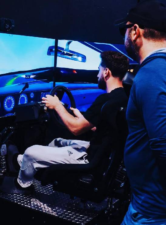 Two men engaged in a racing simulator experience indoors.