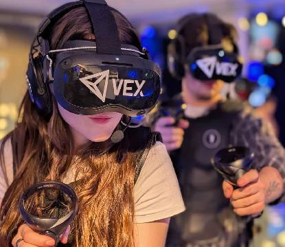 Two people immersed in virtual reality gaming with VR headsets and controllers.